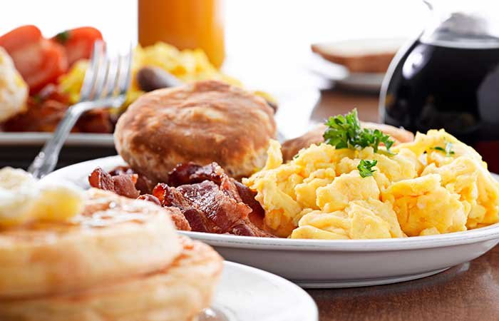 A breakfast plate with scrambled eggs, bacon, and a biscuit, with a stack of waffles in the foreground, typical of a bed and breakfast in Columbia, TN.