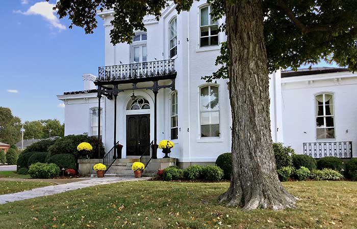 A two-story white bed and breakfast in Columbia, TN, with a black metal balcony above the front entrance and yellow potted chrysanthemums on the porch steps.
