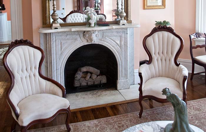 Two cream-colored, high-backed upholstered chairs with wooden frames placed in front of a white marble fireplace at a bed and breakfast in Columbia, TN.