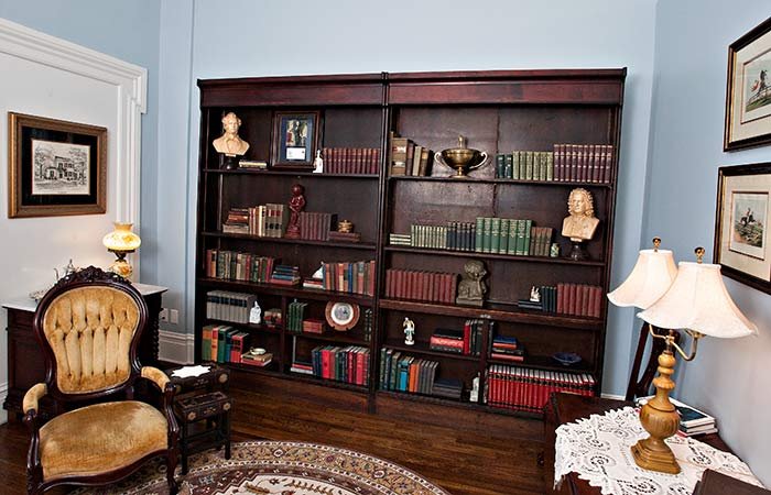 Two large, dark wood bookshelves filled with books and decorative statues in a cozy Columbia, TN bed and breakfast, featuring a velvet armchair and a table lamp.