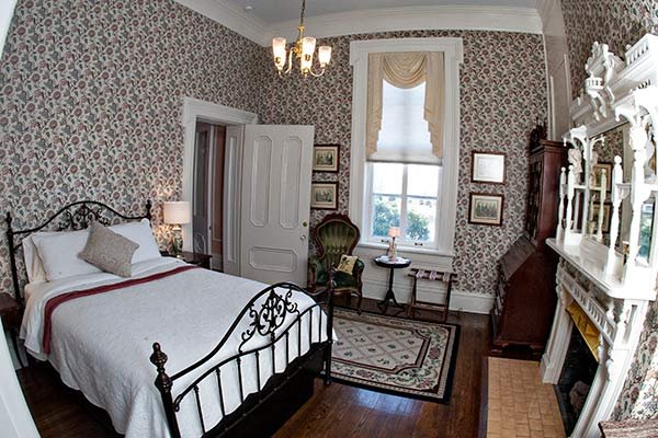 A bedroom at a bed and breakfast in Columbia, TN, featuring floral wallpaper, a black iron bed frame, a green armchair, and a fireplace with an ornate mantel.