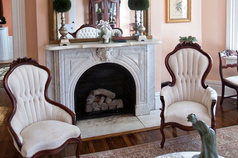 Two ornate, tufted-back cream chairs placed on either side of a marble fireplace at the Blythewood Inn in Columbia, TN.