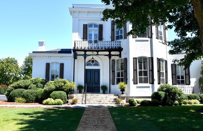 A white two-story historic bed and breakfast in Columbia, TN, with dark shutters, a front porch with a black wrought-iron railing, and a stone walkway leading to the front door.