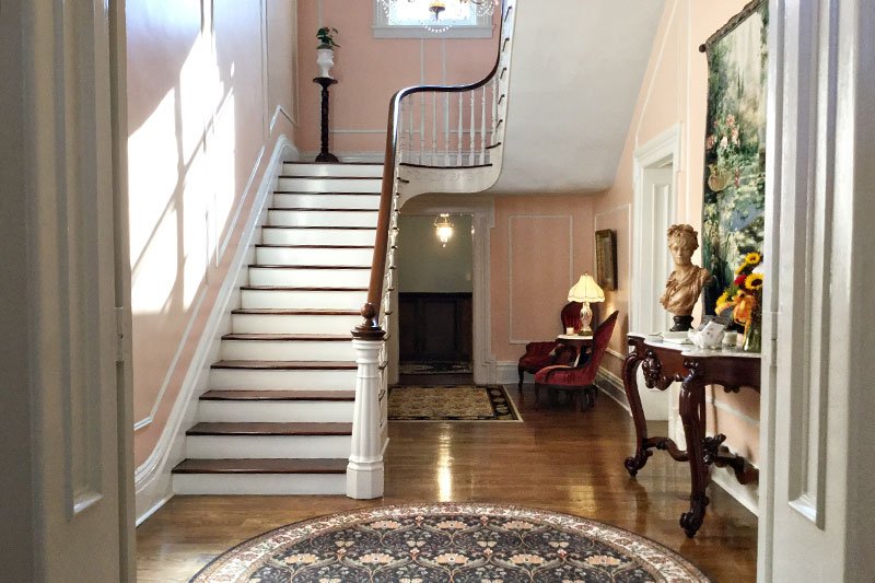 An entryway with a central staircase, light pink walls, and a round patterned rug on the hardwood floor of this special events venue in Columbia, TN.